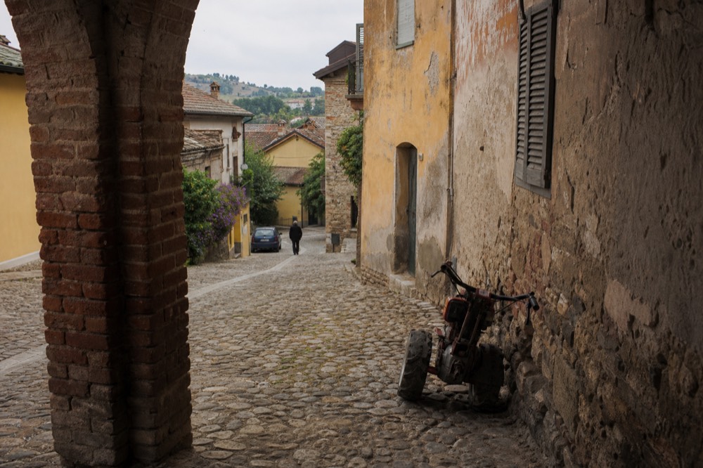 A quiet village street in the Monferrato hills with a bicycle leaning against a stone wall.