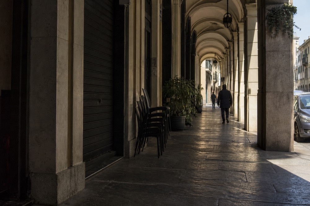 Turin's arcaded shopping street with sunlight falling across the columns.