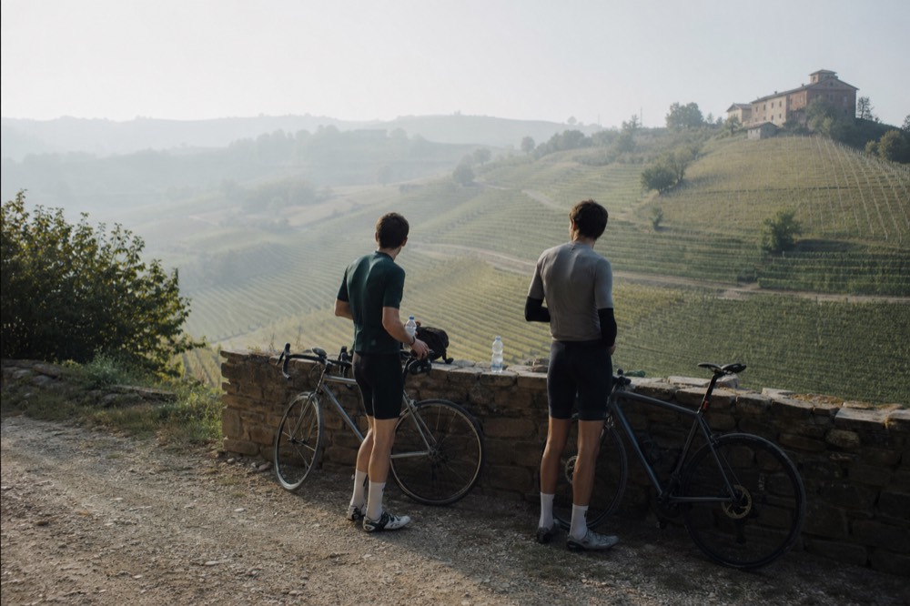 Cyclists resting beside a country road between Langhe vineyards.