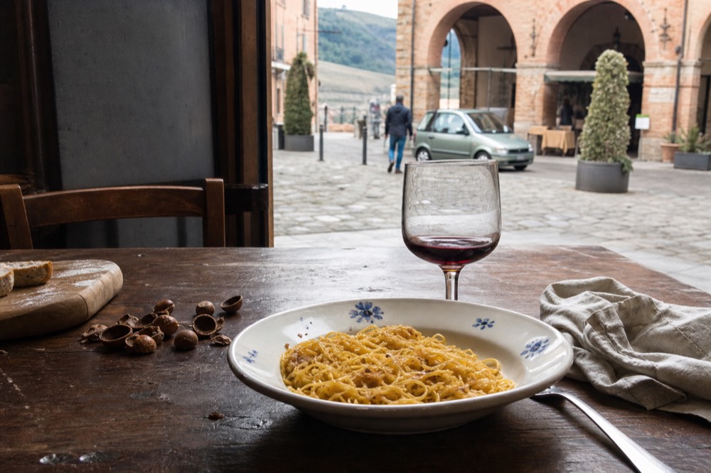 Rustic table with fresh tajarin pasta, hazelnuts and a glass of red wine.