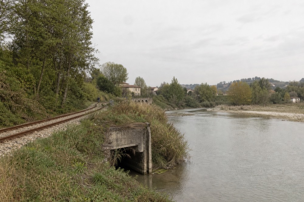 Single-track rail line running beside a calm river through open countryside.